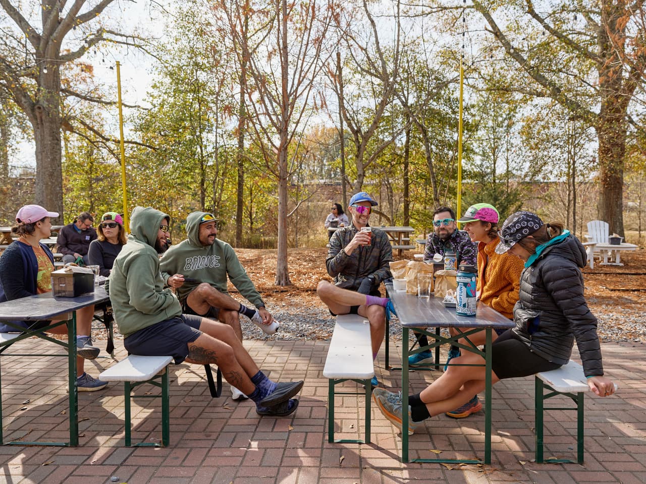 A group of people sit at picnic tables, eating, drinking, and laughing.