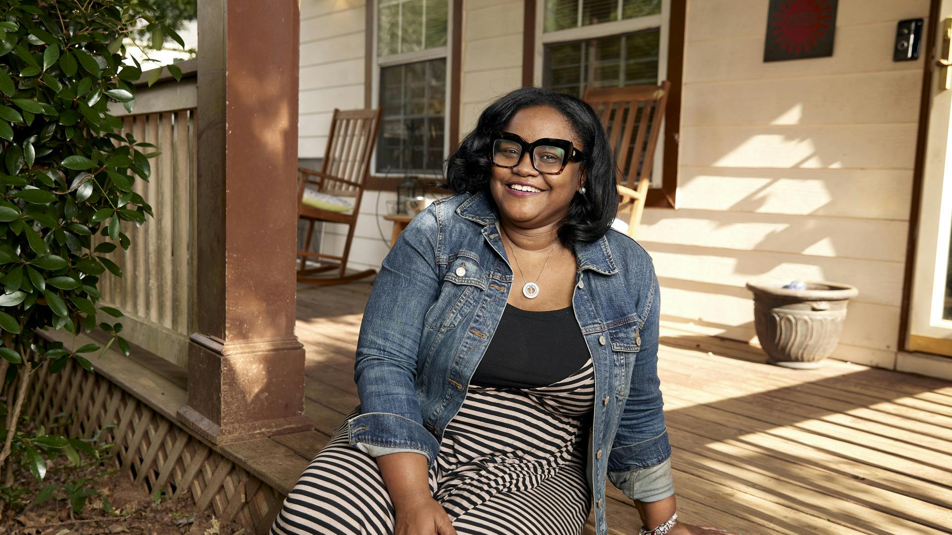 A woman sits on her front porch smiling.