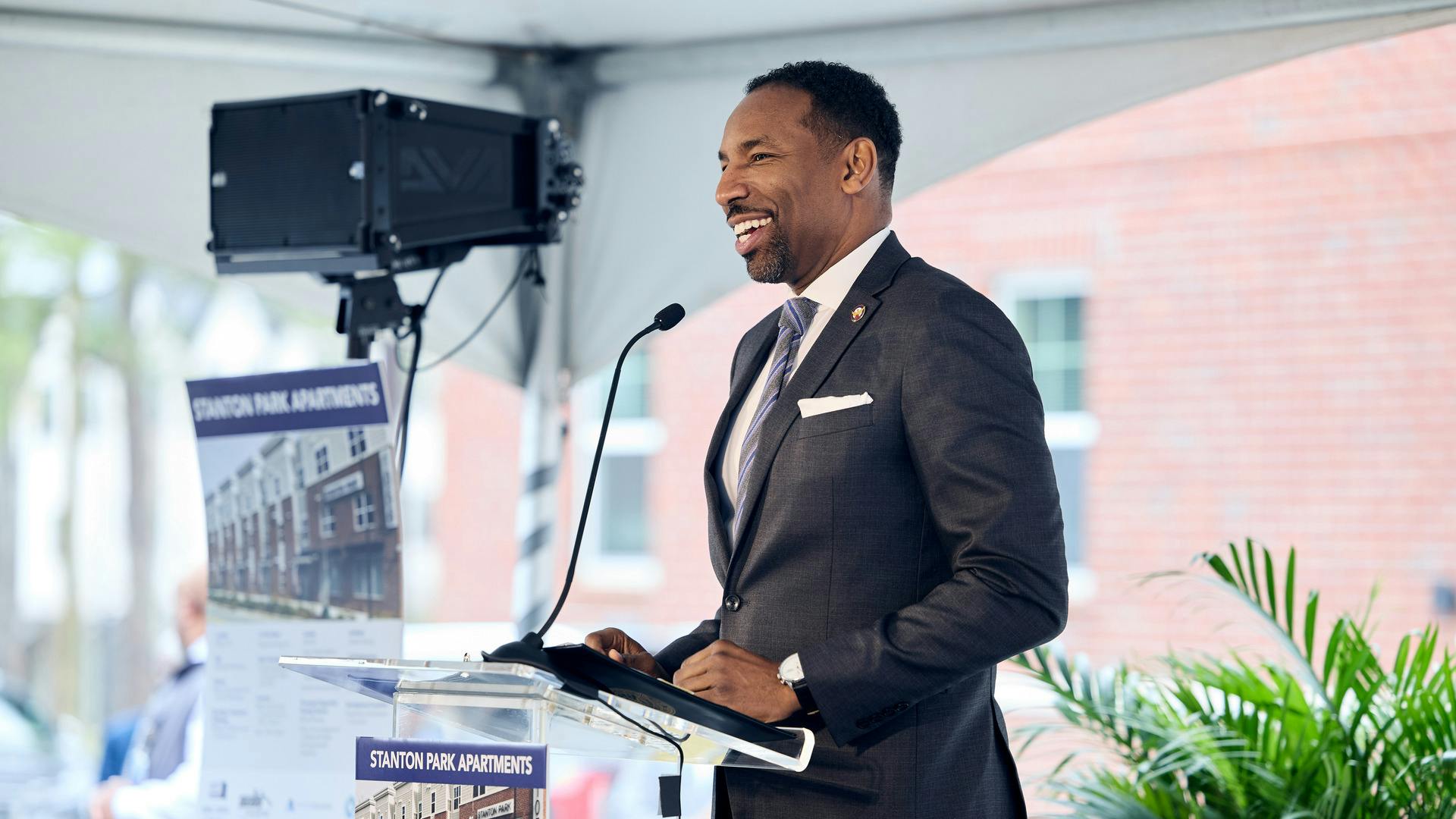 Mayor Andre Dickens stands at a podium in a suit, speaking to a crowd and smiling.