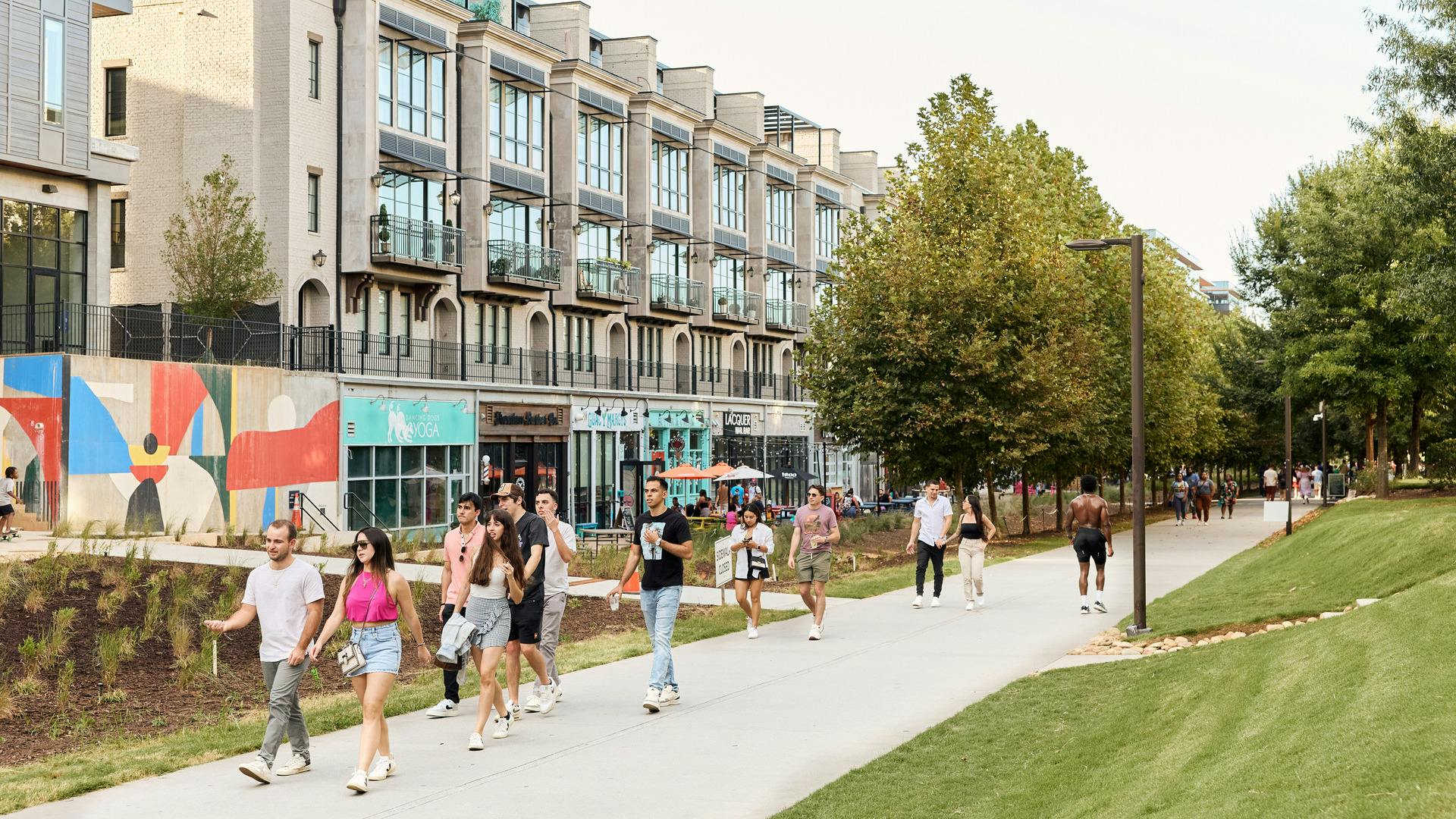 People walk along a trail surrounded by buildings and greenery.