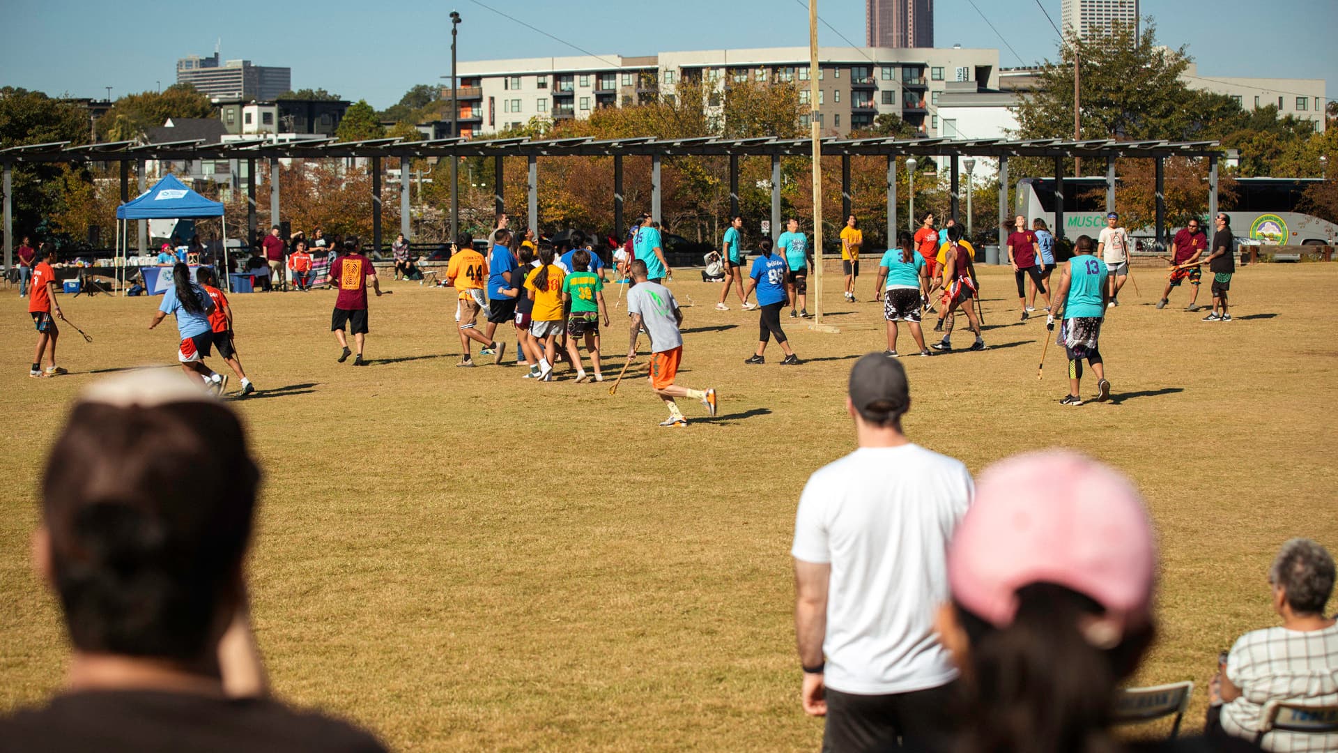 A group of people play Stickball on a field while spectators watch on.