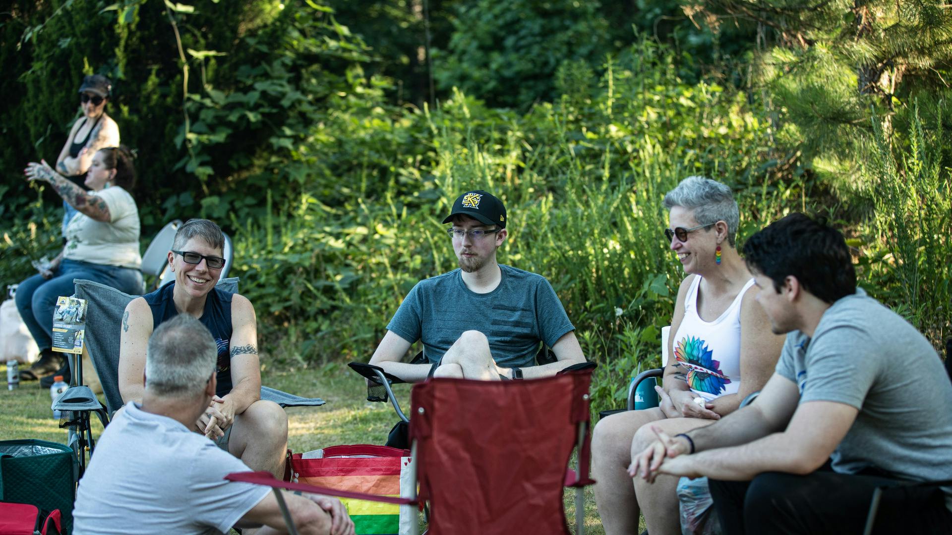 People sit in camping chairs, smiling and talking.