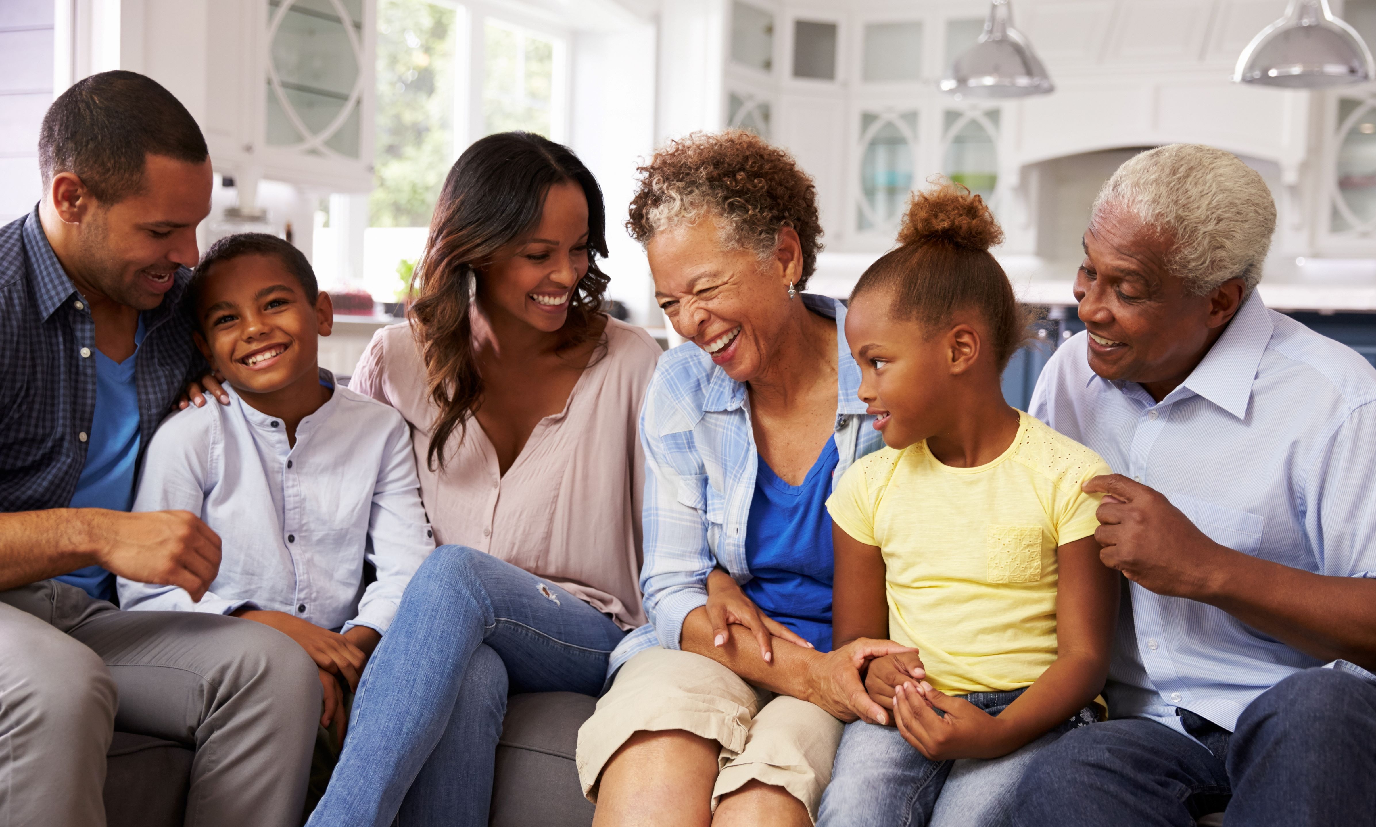 Family of grandparents, parents, and grandkids sitting on a couch smiling