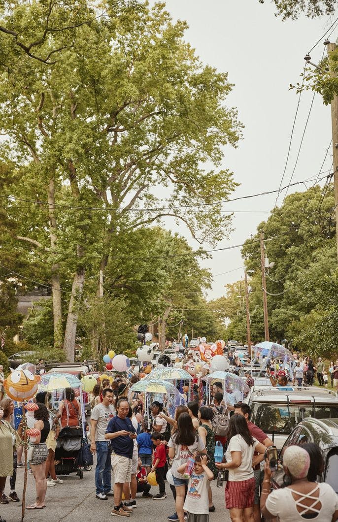 A crowd of people stand on the street with colorful homemade lanterns.